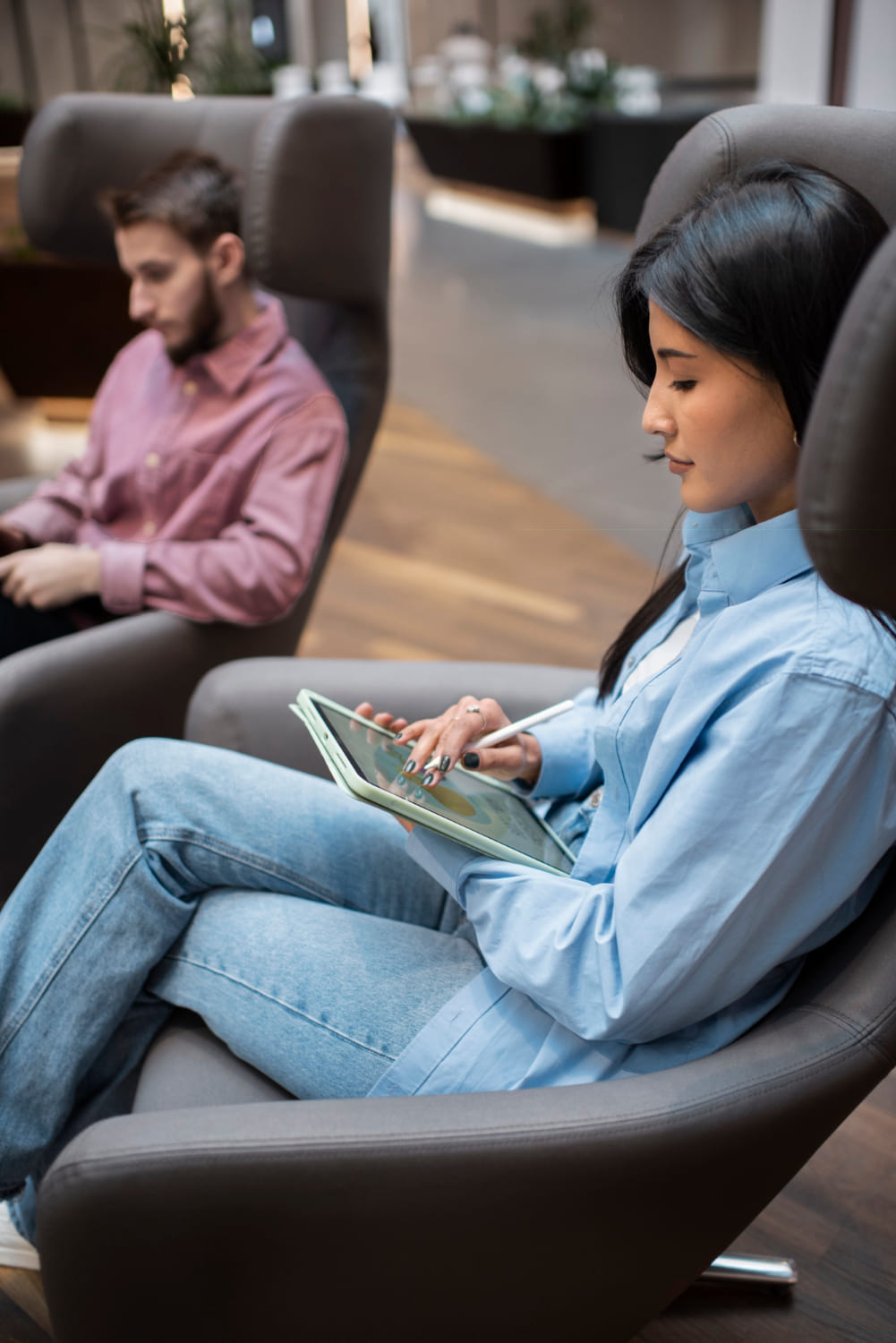 Woman sitting in a modern waiting area using a tablet, representing convenient telehealth access at Abroi Psychiatry