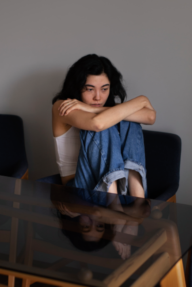 Woman sitting with arms crossed looking downward, representing mental health struggles