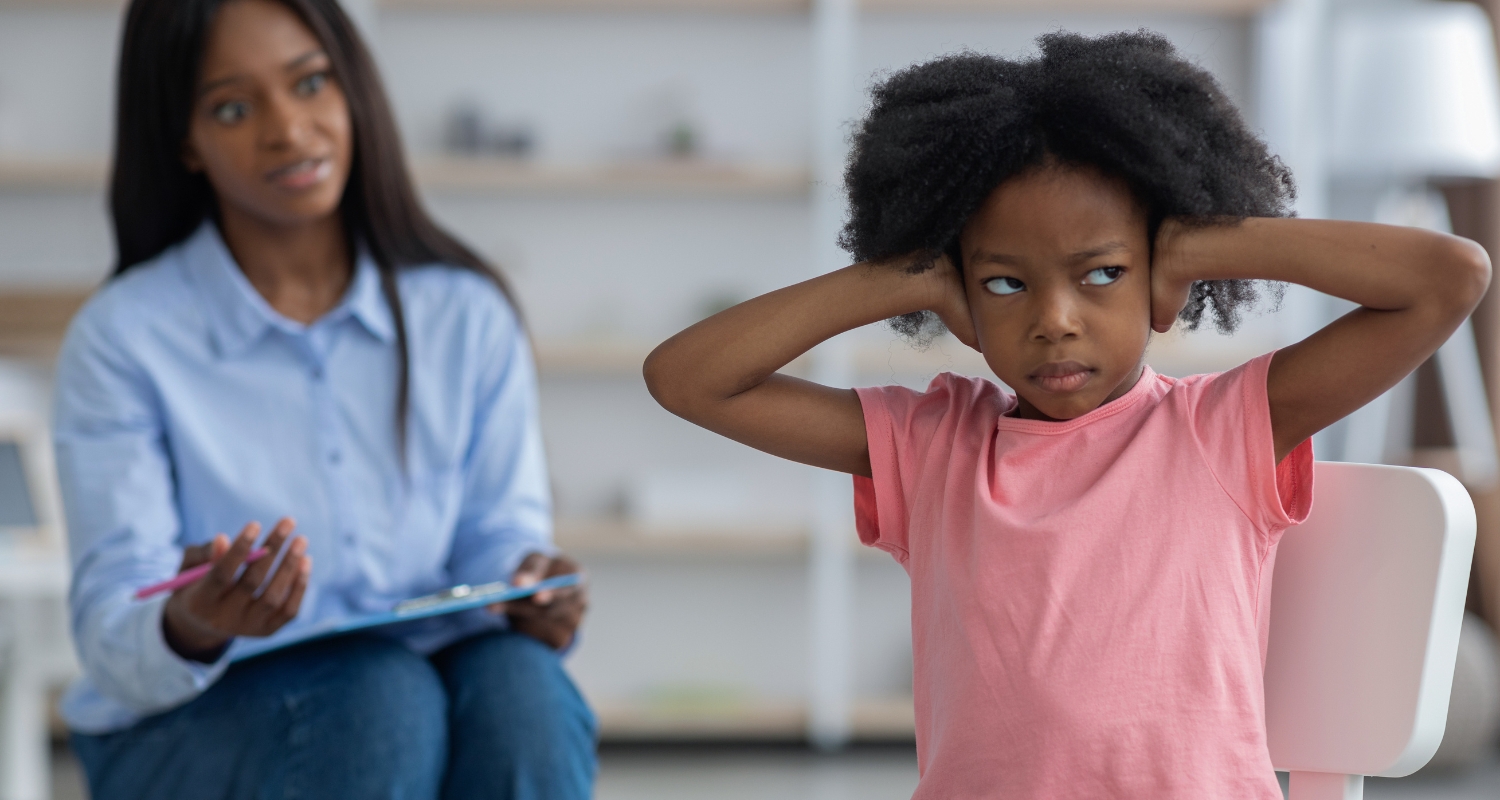 Child with hands on head looking upset while a therapist takes notes in the background, representing adjustment disorder treatment