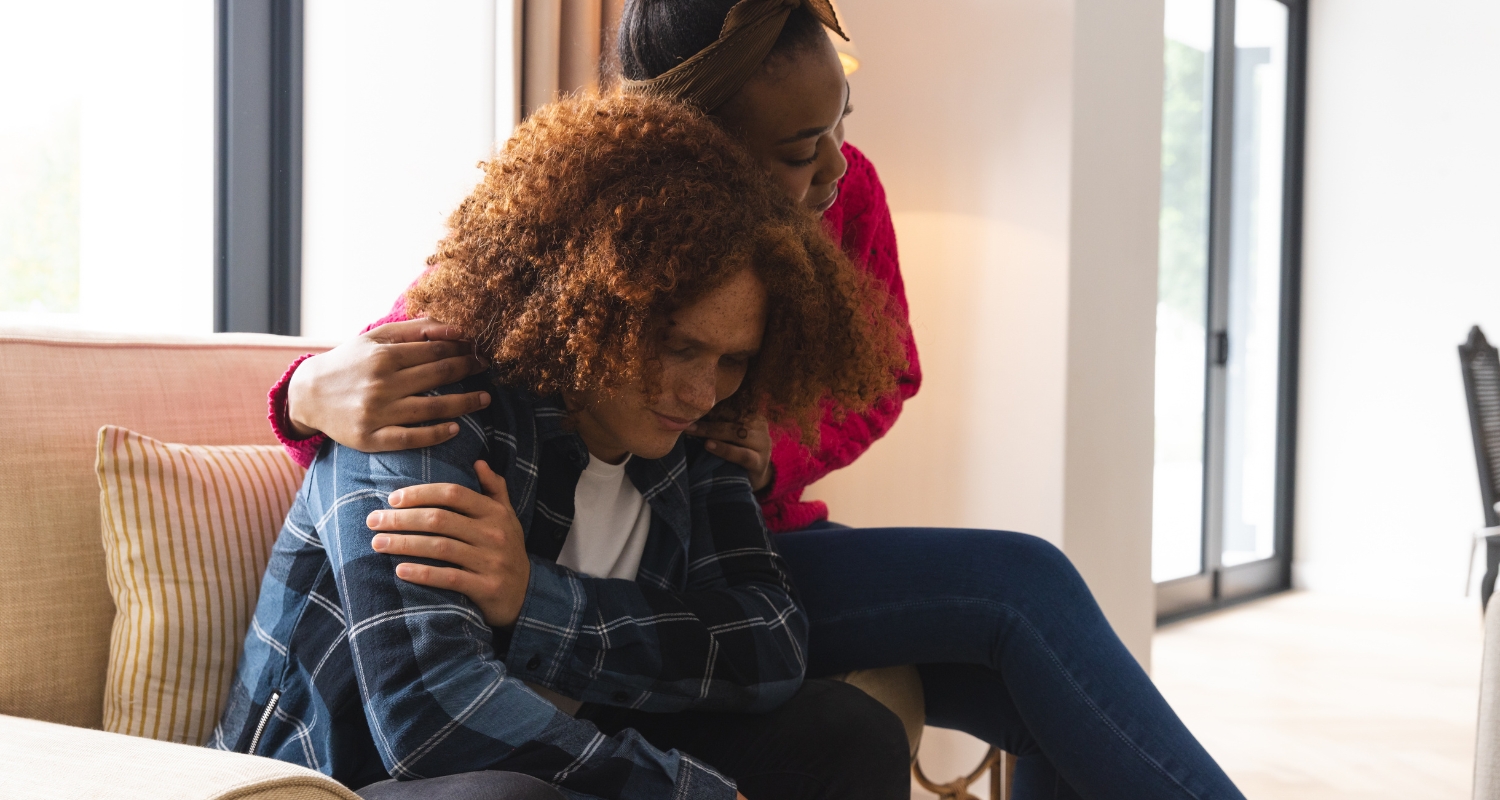 Person sitting with head down being comforted by another, representing grief and loss support