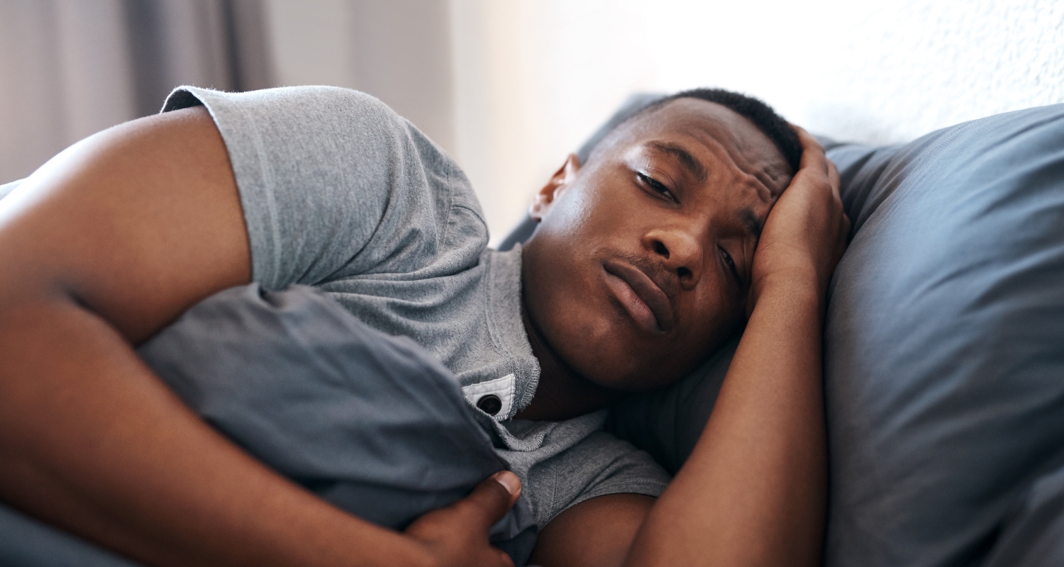 Man lying in bed awake with hand on head, representing insomnia and sleep problems