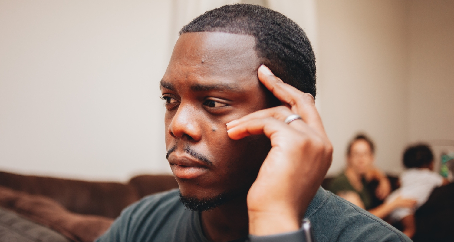 Man sitting with hand to temple looking distressed, representing trauma and PTSD symptoms