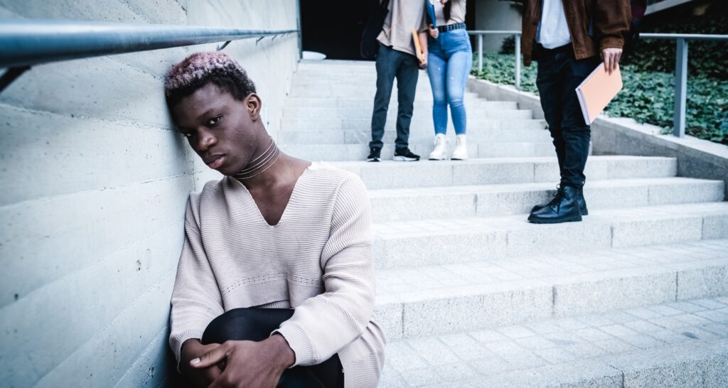 Young man sitting alone on steps while others pass by, illustrating isolation associated with depression