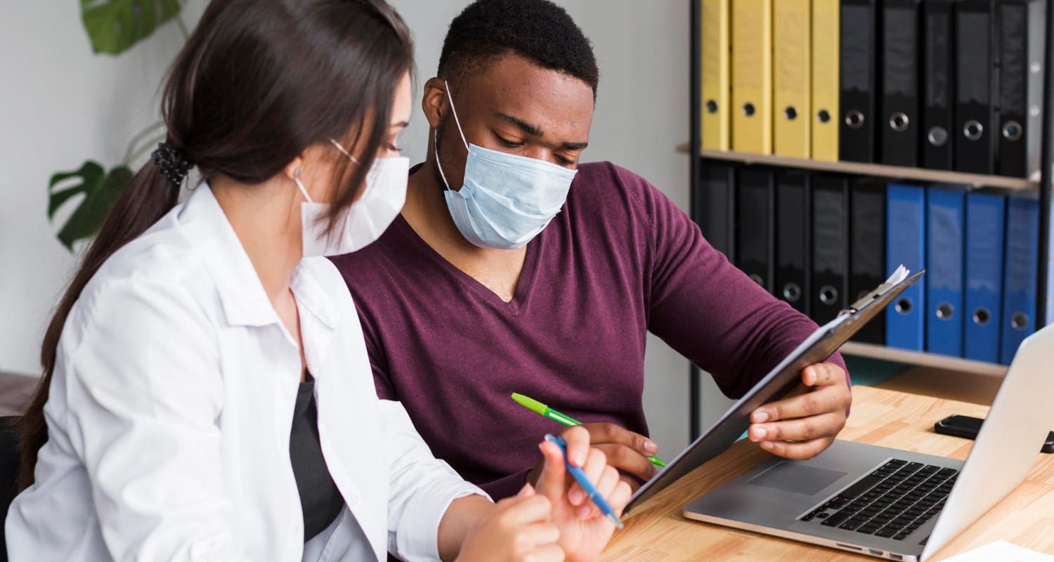 Healthcare provider reviewing a tablet with a masked patient in a clinic setting, representing psychiatric medication management