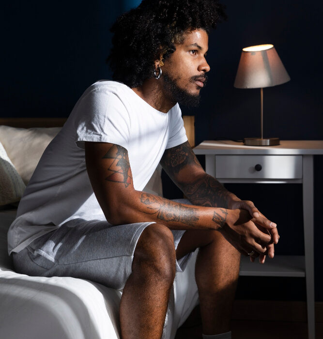 Man sitting on the edge of a bed at night looking pensive, representing mental health struggles and the need for psychiatric support
