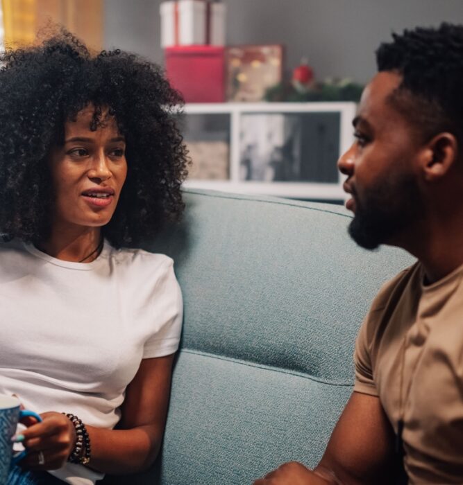 Couple sitting on a couch having a serious conversation, representing relationship stress and life stressors
