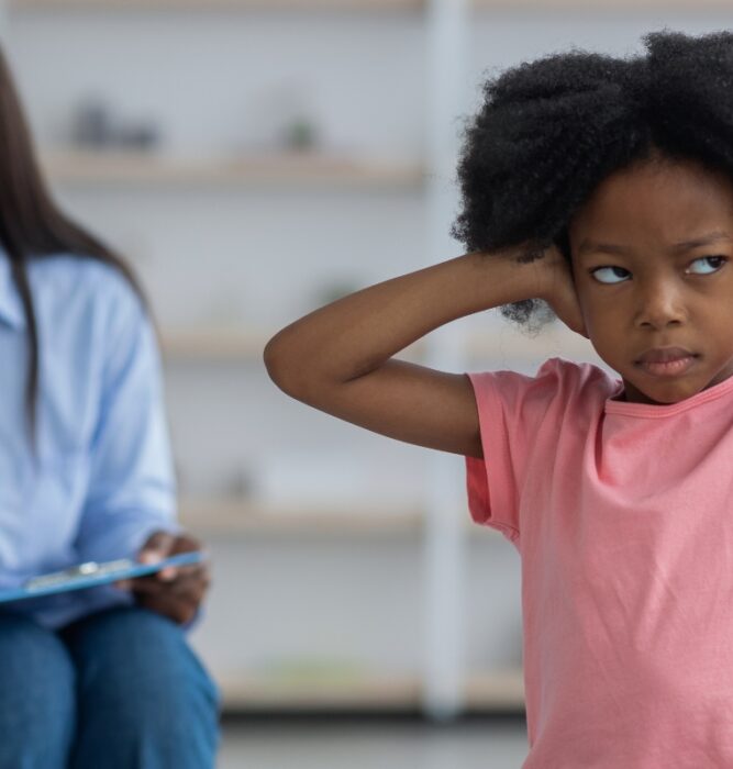 Child with hands on head looking upset while a therapist takes notes in the background, representing adjustment disorder treatment