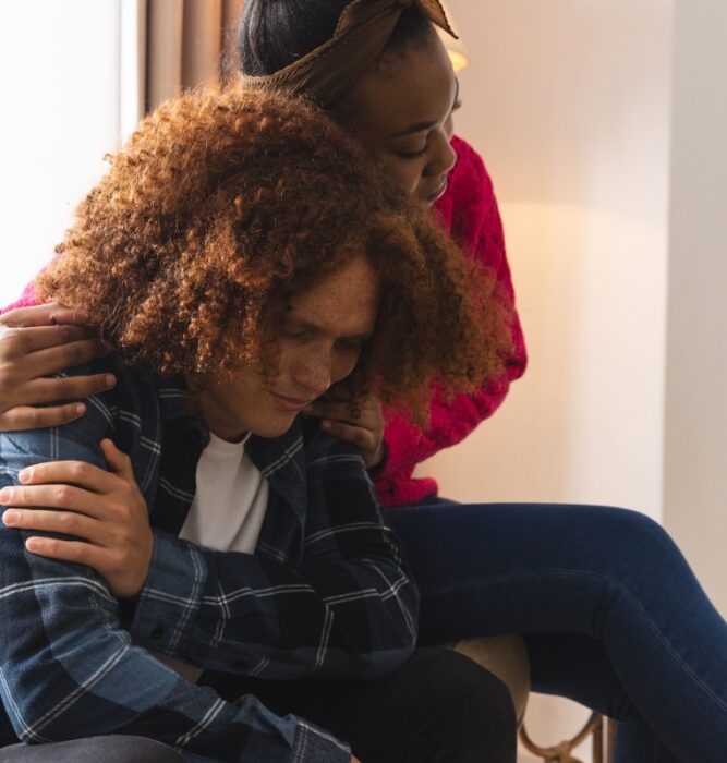 Person sitting with head down being comforted by another, representing grief and loss support